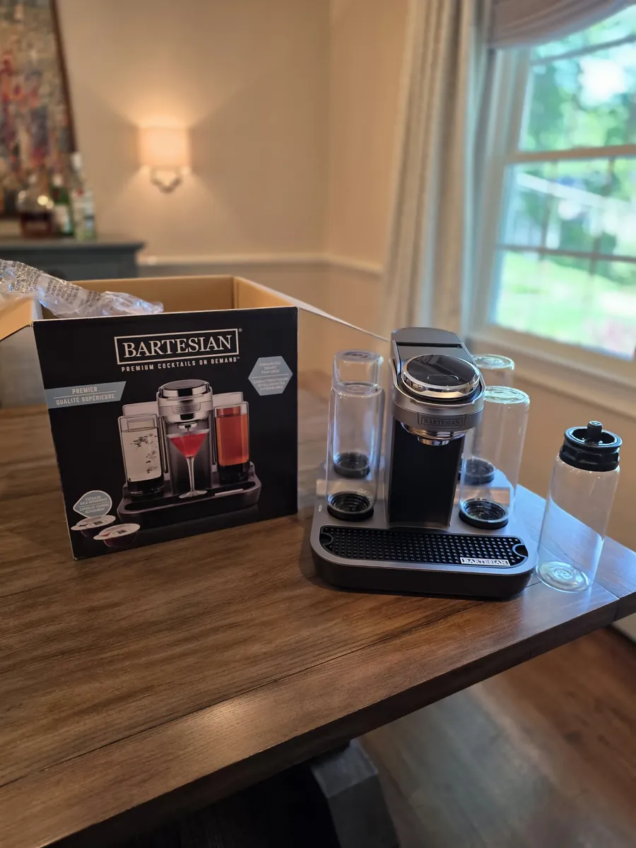 Bartesian Premier cocktail machine beside its retail box on a wood table, with glass spirit bottles in place